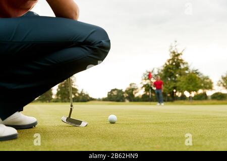 Close Up Of Female Golfer Lining Up Shot On Putting Green As Man Tends Flag Stock Photo