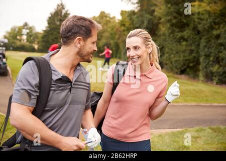 Mature Couple Playing Round Of Golf Carrying Golf Bags And Talking Stock Photo