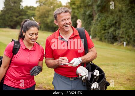 Mature Couple Playing Round Of Golf Carrying Golf Bags And Marking Scorecard Stock Photo