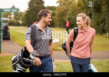 Mature Couple Playing Round Of Golf Carrying Golf Bags And Talking Stock Photo