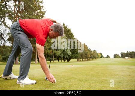 Mature Male Golfer Preparing To Hit Tee Shot Along Fairway With Driver Stock Photo