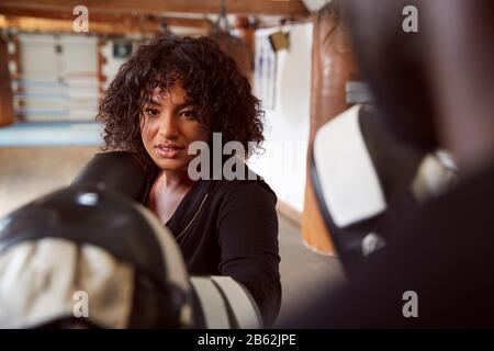 Male Personal Trainer Sparring With Female Boxer In Gym Using Training Gloves Stock Photo