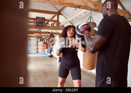 Male Personal Trainer Sparring With Female Boxer In Gym Using Training Gloves Stock Photo