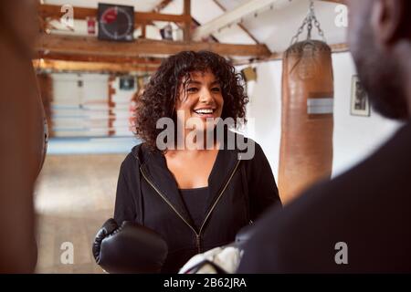 Male Personal Trainer Sparring With Female Boxer In Gym Using Training Gloves Stock Photo