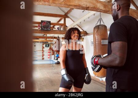 Male Personal Trainer Sparring With Female Boxer In Gym Using Training Gloves Stock Photo