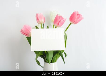 Flowers mock up congratulation. Congratulations card in bouquet of pink tulips on white background. White blank card with space for text, frame mockup Stock Photo
