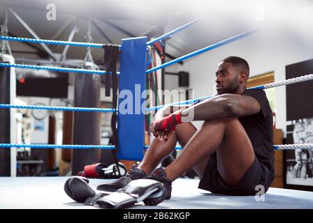 Tired Male Boxer Sitting In Boxing Ring In Gym After Training Session Stock Photo