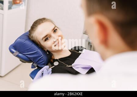 Young female sitting in dentist office and looking at her doctor with smile. The woman came to see the dentist. Happy patient and dentist concept. Stock Photo