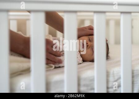 Lovely newborn baby girl sleeping in bed, view through crib bars Stock Photo