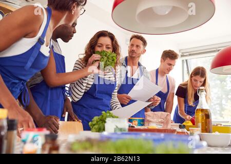 Male And Female Adult Students Looking At Recipe And Smelling Ingredients In Cookery Class Stock Photo