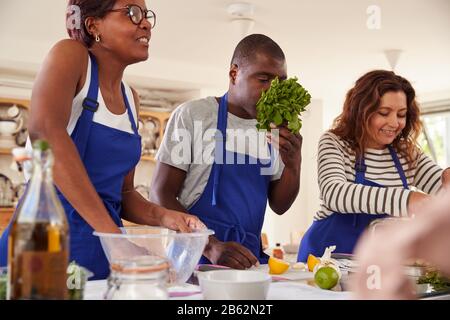 Male And Female Adult Students Smelling Ingredients In Cookery Class Stock Photo