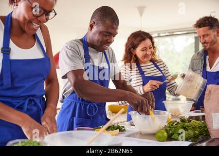 Male And Female Adult Students Preparing Ingredients For Dish In Kitchen Cookery Class Stock Photo