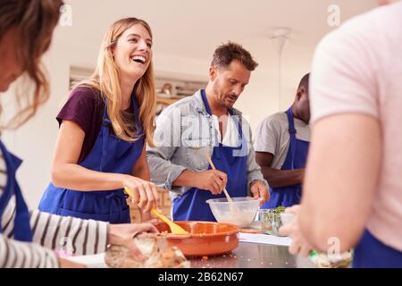 Male And Female Adult Students Preparing Ingredients For Dish In Kitchen Cookery Class Stock Photo