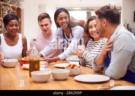 Group Of Friends Sitting Around Table Eating Meal At Home Together Stock Photo