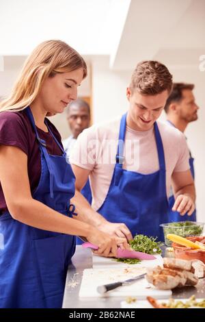 Male And Female Adult Students Preparing Ingredients For Dish In Kitchen Cookery Class Stock Photo