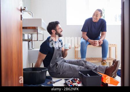 Male Plumber With Female Apprentice Taking A Break From Fixing Leaking Sink In Home Bathroom Stock Photo