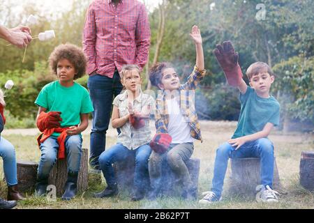 Team Leader With Group Of Children On Outdoor Activity Trip Toasting Marshmallows Over Camp Fire Stock Photo