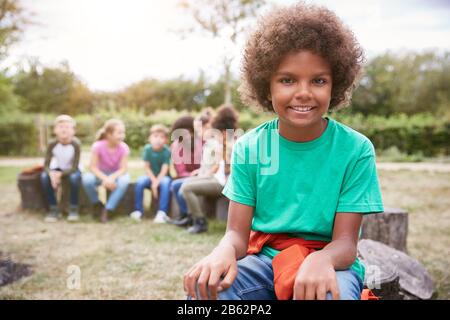 Portrait Of Boy On Outdoor Activity Camping Trip Sitting Around Camp Fire With Friends Stock Photo