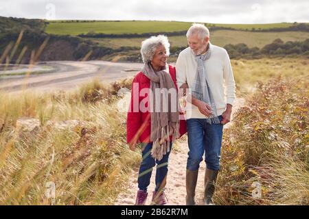 Loving Active Senior Couple Walking Arm In Arm Through Sand Dunes On Winter Beach Vacation Stock Photo