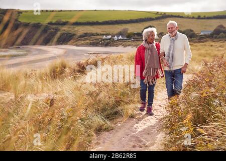 Loving Active Senior Couple Walking Arm In Arm Through Sand Dunes On Winter Beach Vacation Stock Photo