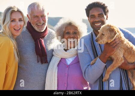 Portrait Of Senior Couple Walking Along Shoreline With Adult Offspring And Dog On Winter Beach Vacation Stock Photo
