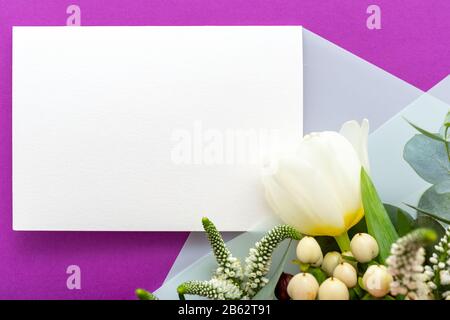 Flowers mock up wedding invitation. Congratulations card in bouquet of white flowers tulips, eucalyptus on purple background. Blank card, space for Stock Photo