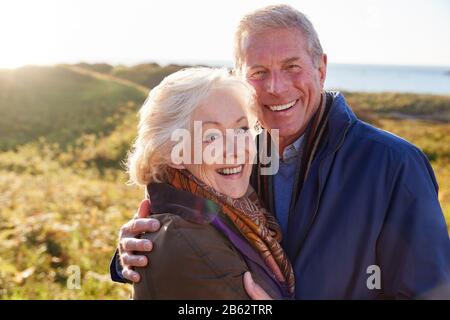Portrait Of Loving Active Senior Couple Walking Along Coastal Path In Autumn Together Stock Photo
