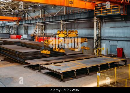 Overhead crane with electromagnetic beam grippers lifting steel sheets. Stock Photo