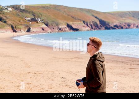 Young Man Flying Drone With Camera On Beach With Waves In Background Stock Photo