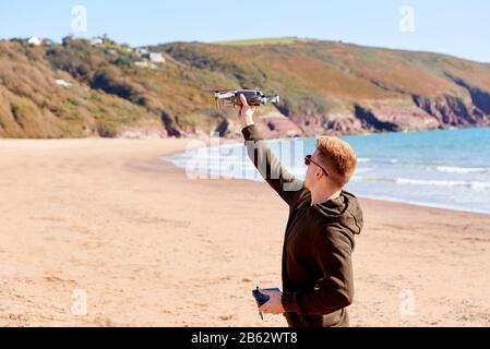 Young Man Flying Drone With Camera On Beach With Waves In Background Stock Photo