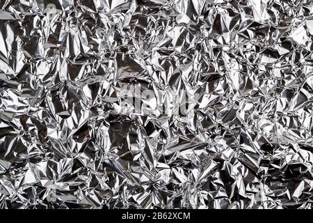 Crumpled aluminum foil texture. Sheet of creased silver foil with shiny folds for background. Metal wrinkled surface as graphic resource. Top view. Stock Photo