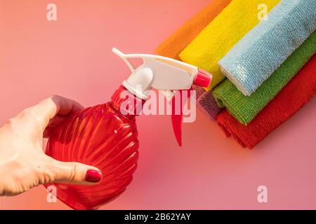 protective latex rubber gloves holding towel and bottle of cleaning detergent spray for windows and glass in her hand isolated on pastel pink Stock Photo