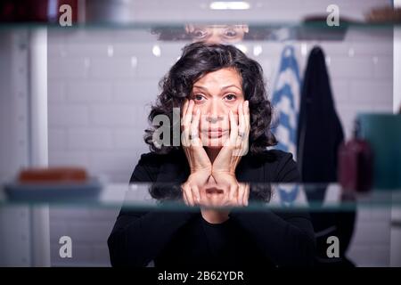 View Through Bathroom Cabinet Of Unhappy Mature Businesswoman Getting Ready For Work Stock Photo
