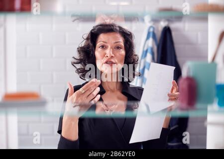 View Through Bathroom Cabinet Of Mature Businesswoman Practising Presentation Stock Photo