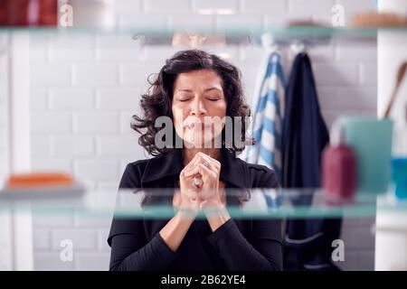 View Through Bathroom Cabinet Of Mature Businesswoman Praying Stock Photo