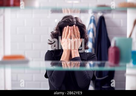 View Through Bathroom Cabinet Of Unhappy Mature Woman Covering Face With Hands Stock Photo