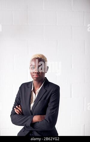 Portrait Of Determined Young Businesswoman Wearing Suit Standing Against White Studio Wall Stock Photo