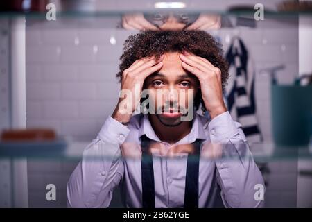 View Through Bathroom Cabinet Of Unhappy Young Businessman Getting Ready For Work Stock Photo