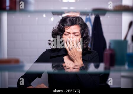 View Through Bathroom Cabinet Of Mature Businesswoman Yawning In Morning Stock Photo