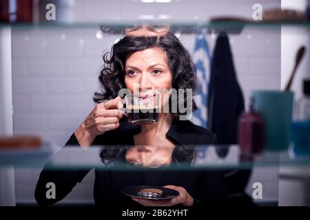 View Through Bathroom Cabinet Of Mature Businesswoman Drinking Coffee Stock Photo