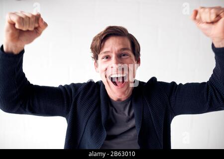 Happy Man Wearing Casual Clothing Celebrating Standing Against White Studio Wall Stock Photo