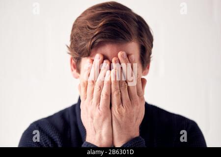 Studio Shot Of Unhappy Man Covering Face With Hands Stock Photo
