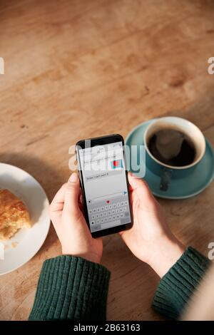 Close Up Of Woman Looking At Messages Arranging Romantic Date On Mobile Phone Messaging App In Cafe Stock Photo