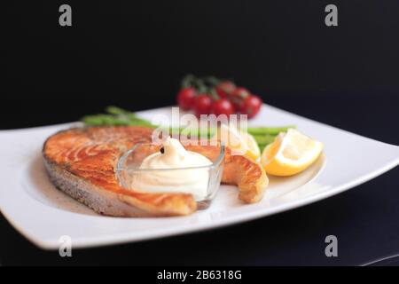salmon steaks with vegetables and spices: asparagus, tomatoes, ginger, pepper corns, salt, chili, onion, lemon and olive oil on black background. Heal Stock Photo