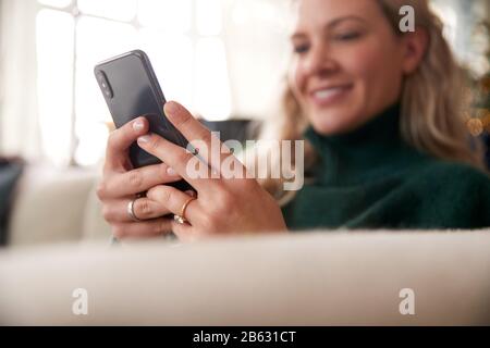 Close Up Of Woman Relaxing On Sofa At Home Using Mobile Phone Stock Photo
