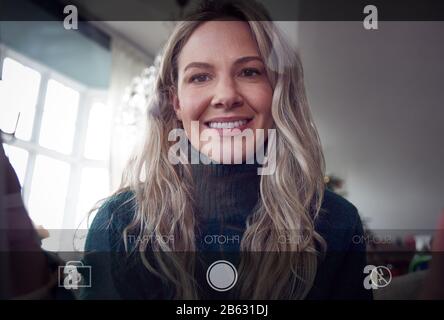 View From Behind Mobile Phone Screen As Woman Takes Selfie At Home Stock Photo