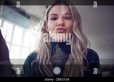 View From Behind Mobile Phone Screen As Woman Takes Selfie At Home Stock Photo
