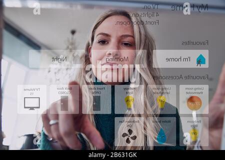 View From Behind Mobile Phone Screen As Woman Uses Home Security App Stock Photo