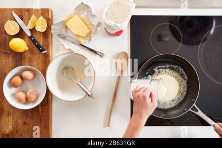 Overhead Shot Of Woman In Kitchen Pouring Batter Into Pan For Pancakes Or Crepes For Pancake Day Stock Photo