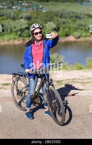Adult attractive female cyclist stand near bicycle and makes the photo by smart phone. Stock Photo